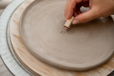 Seramik atölyesinde kil ürünleri özel paternlerle ve sembollerle süslemek. Bir çömlek projesine mektup ve süs kazımak için kilden bir pul kullanmak.