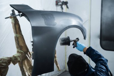 Tamirci garajdaki boya spreyiyle arabanın rengini düzeltiyor. Araba boyacısı arabanın kaputunu koyu renge boyuyor.