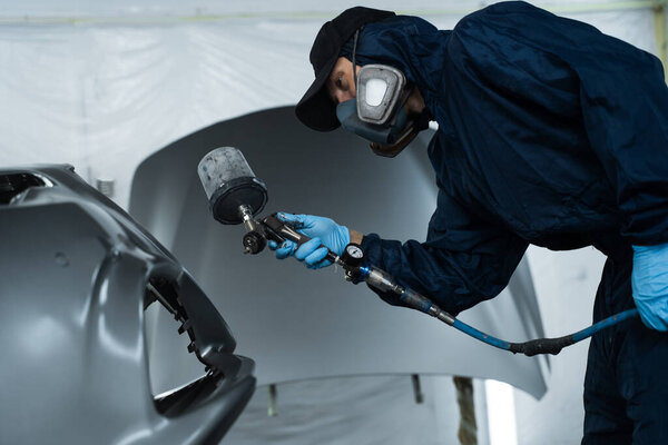 Рабочий рисует машину тёмным цветом с помощью спрея HVLP. Автомеханик меняет цвет автомобиля с помощью губки и распылителя краски