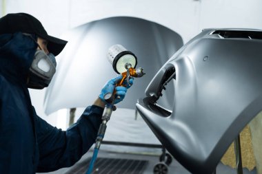 Yüzeye pürüzsüz bir görünüm vermek için metalin üzerine cam yapıştırıyorum. Koruyucu maske takan ve eldiven takan işçiler, LVLP sprey tabanca kullanarak arabaya lakquer uyguluyorlar.