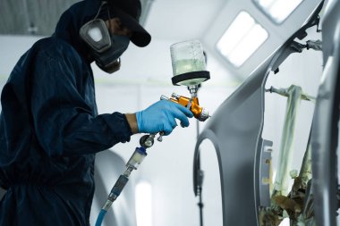 Araba boyacısı boya işini boya püskürtücüsüyle boyayarak bitiriyor. LVLP sprey tabancasını metal üzerine yaymak için kullanıyor.