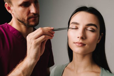 BlePharoplasti. Cerrah göz kapağındaki noktalı çizgiler arasındaki mesafeyi anatomik cımbızla kontrol ediyor. Üst blefaroplasti işaretleme göz kapağı