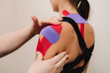 Atlet performansını arttırmak için boynunda ve omuzlarında ince, esnek bantlar olan genç bir kadın. Doktor kasları çalıştırmak için hastanın omzuna kineziyoloji bantları takıyor.