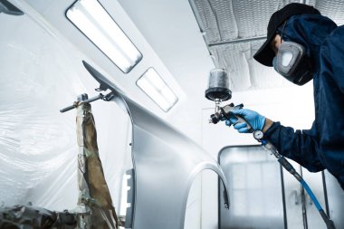 İşçi arabayı HVLP sprey tabancasıyla koyu renklere boyuyor. Otomobil tamircisi, aracın rengini sünger ve boya spreyi kullanarak değiştiriyor