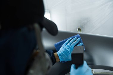 Zararları önlemek için statik tabanca kullanmak ve arabayı boyayla kaplamadan önce tozu silmek. Tamirci, metali boyacıya hazırlamak için statik silahlarla çalışıyor.