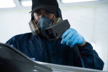 Zararları önlemek için statik tabanca kullanmak ve arabayı boyayla kaplamadan önce tozu silmek. Tamirci, metali boyacıya hazırlamak için statik silahlarla çalışıyor.