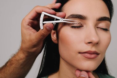 Göz kapaklarını düzeltmek için birofaroplasti hazırlıyorum. Üst blefaroplasti. Plastik cerrah, Castroviejo kalibreli hastasının gözünün içindeki cerrahi mesafeyi ölçüyor.