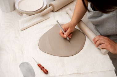 Preparing clay for cutting and assembling it. Slab building method in ceramics crafting. Using a wooden stick to roll out a flat sheet of clay clipart