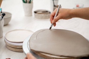 Kız kilden yuvarlak bir şekil alıyor. Keskin bir çömlek bıçağı kullanarak kilden mükemmel yuvarlak bir şekil çıkarmışlar. Seramik sınıfı.