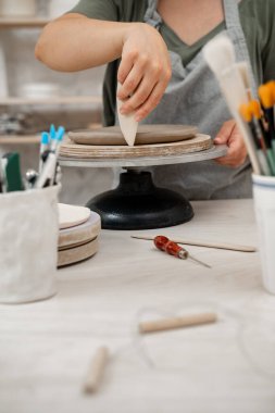 Kız kilden bir ürünün kenarlarını yumuşatmak için çömlekçi kullanıyor. Kil kazıyıcı ile pürüzsüz açı dönüşümü ve desenli kaburgalar.