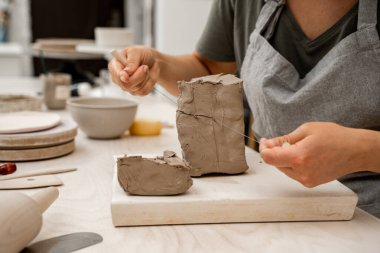 Kız, ürünü modellemeden önce bir parça kil kesmek için tel kesici kullanıyor. Keskin bir tel kil kesici kullanarak büyük bir bloktan bir parça kil kesmek.