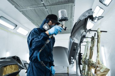 İşçi arabayı HVLP sprey tabancasıyla koyu renklere boyuyor. Otomobil tamircisi, aracın rengini sünger ve boya spreyi kullanarak değiştiriyor