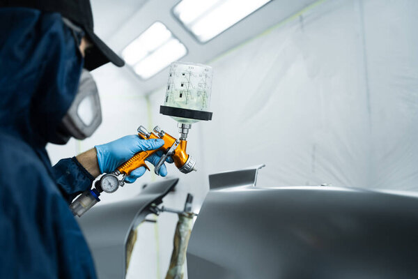 Нанесение лака на металл, чтобы придать поверхности гладкий вид. Работник в защитной маске и перчатках наносит лак на автомобиль с помощью спрея LVLP