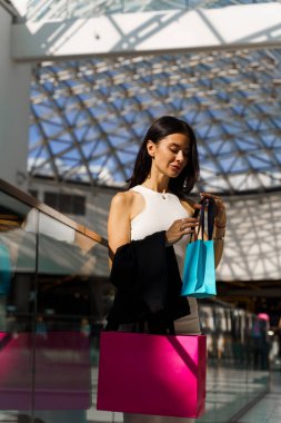 Genç bayan alışveriş merkezinde eğleniyor. Beyaz elbiseli güzel bir kadınla Kara Cuma alışverişi yıldönümü için hediyeler hazırlıyor.