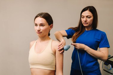 Diyathermi. Acıyı azaltmak ve vücut dokularını iyileştirmek için yüksek frekanslı akımlar kullanmak. Doktor yaralı omzunu iyileştirmek için kadın hastaya tekar terapisi yapıyor.