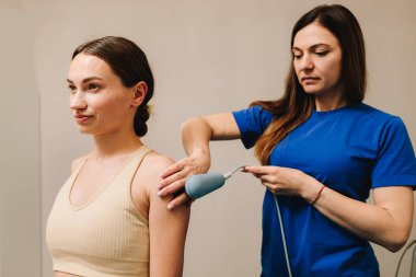 Diyathermi. Acıyı azaltmak ve vücut dokularını iyileştirmek için yüksek frekanslı akımlar kullanmak. Doktor yaralı omzunu iyileştirmek için kadın hastaya tekar terapisi yapıyor.