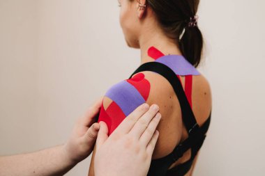 Doktor kasları çalıştırmak için hastanın omzuna kineziyoloji bantları takıyor. Genç kadının boynunda ve omuzlarında atlet performansını arttırmak için ince, esnek bantlar var.