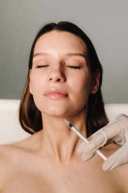 Kozmetik uzmanı kadın çenesine dolgu yapıyor. Yüksek kaliteli bir doktor tarafından çenenin şekli düzeltiliyor. Yüz düzeltmenin güzellik tedavisi