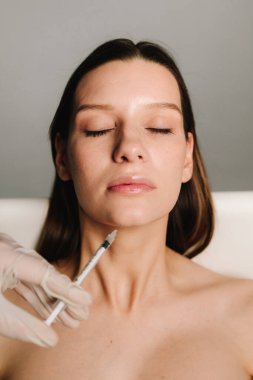 Kozmetik uzmanı kadın çenesine dolgu yapıyor. Yüksek kaliteli bir doktor tarafından çenenin şekli düzeltiliyor. Yüz düzeltmenin güzellik tedavisi