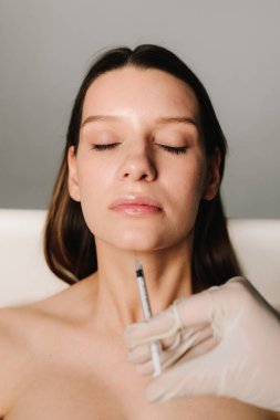 Yüksek kaliteli bir doktor tarafından çenenin şekli düzeltiliyor. Yüz düzeltmenin güzel davranışı. Kozmetik uzmanı kadın çenesine dolgu yapıyor.