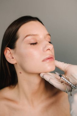 Yüksek kaliteli bir doktor tarafından çenenin şekli düzeltiliyor. Yüz düzeltmenin güzel davranışı. Kozmetik uzmanı kadın çenesine dolgu yapıyor.