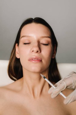 Yüksek kaliteli bir doktor tarafından çenenin şekli düzeltiliyor. Yüz düzeltmenin güzel davranışı. Kozmetik uzmanı kadın çenesine dolgu yapıyor.