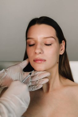 Yüksek kaliteli bir doktor tarafından çenenin şekli düzeltiliyor. Yüz düzeltmenin güzel davranışı. Kozmetik uzmanı kadın çenesine dolgu yapıyor.