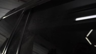 Garaj 4K videosunun yan camını elle temizlemek için arabaya deterjan sıkıyorum. Arabanın yan camlarında mikro fiber bez silme işlemi.