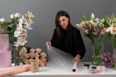 Çiçekçi çiçek aranjmanı için ambalaj kağıdını makasla kesiyor. Çiçek buketi yapmak için çiçek süsleme hazırlıyorum.