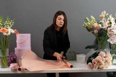 Çiçekçi çiçek aranjmanı için ambalaj kağıdını makasla kesiyor. Çiçek buketi yapmak için çiçek süsleme hazırlıyorum.