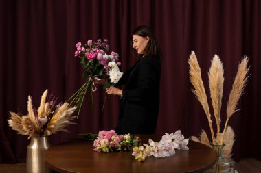 Kadın çiçekçi, arka planda buket oluşturuyor. Çiçekçi kadın, müşteriler için çiçek dekoru hazırlıyor.