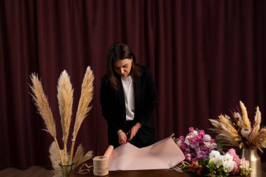 Çiçekçide çiçekçiden karışık çiçeklerden bir buketi paket kağıdına sarmak. Çiçekçi müşteriye güllerden ve karanfillerden bir kompozisyon yapar.