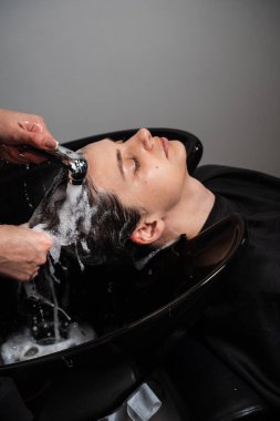 Bir kuaförün dükkanında fazla yağ ve kiri profesyonelce yıkamak. Kuaför müşterinin esmer saçındaki şampuanı yıkıyor.