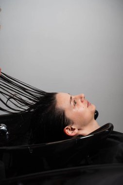 Bir kuaförün dükkanında fazla yağ ve kiri profesyonelce yıkamak. Kuaför müşterinin esmer saçındaki şampuanı yıkıyor.