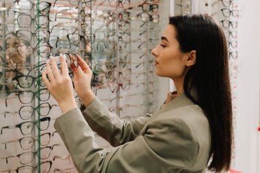 Farklı çerçeveli geniş bir gözlük seçimi. Temiz lensli yüksek kalite gözlük. Kadın istemci optik mağazadaki gözlüklerden gözlük seçer.