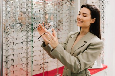 Kadın müşteri optik mağazadaki stanttan gözlük seçiyor. Farklı çerçeveli geniş bir gözlük seçimi. Temiz lensli yüksek kalite gözlük.