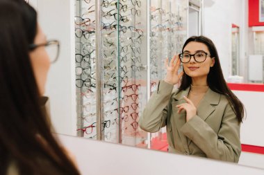 Kadın alışveriş merkezinin gözlükçü köşesinde gözlük seçmeye çalışıyor. Optik mağazada saydam lensli gözlük seçmek