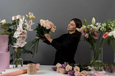 Gri arka plan çiçek stüdyosundaki çiçekçinin pembe güllerinden buket yapıyorum. Özel sipariş için çiçek bileşimi toplanıyor