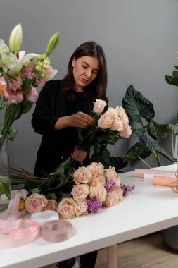 Özel sipariş için çiçek bileşimi topluyorum. Gri arka plan çiçek stüdyosunda çiçekçinin pembe güllerinden buket hazırlıyorum.