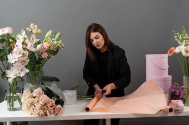 Çiçek buketi yapmak için çiçek süslemesi hazırlıyorum. Çiçekçi çiçek aranjmanı için makas ile ambalaj kağıdı kesiyor.