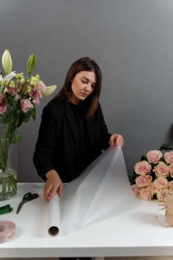 Çiçekçi çiçek aranjmanı için ambalaj kağıdını makasla kesiyor. Çiçek buketi yapmak için çiçek süsleme hazırlıyorum.