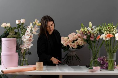 Çiçekçinin masasında gül çiçeklerini kağıda sarmak. Çiçek buketini düzenleyen bir çiçekçi.