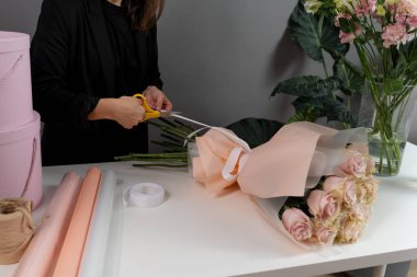 Çiçekçi çiçekçi dükkanındaki siparişe kurdele ile bir çiçek aranjmanı bağlıyor. Teslimat için güllerden taze buket yapıyorum.