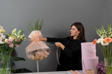 Teslimat için güllerden taze buket yapıyorum. Çiçekçi çiçekçi dükkanındaki siparişe bir çiçek aranjmanı bağlıyor.