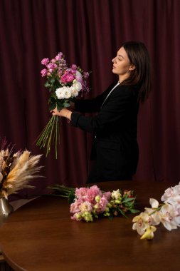 Teslimat için taze çiçek buketi yapıyorum. Çiçekçi çiçekçi dükkanındaki siparişe bir çiçek aranjmanı bağlıyor.