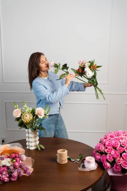 Beste yapmadan önce taze çiçekler hazırlıyorum. Kadın çiçekçi elinde bir buket kompozisyon tutuyor ve dizayn ediyor. Stüdyoda çiçek buketi yapan çiçekçi.