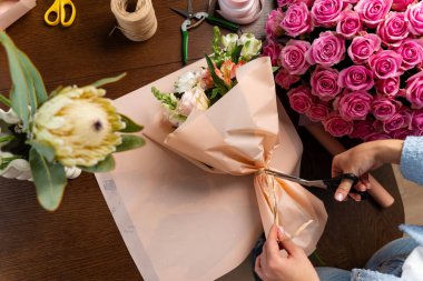 Çiçekçi tarafından çiçekçide bir buket karışık çiçek oluşturuluyor. Buket kompozisyonunu güzel taze çiçeklerle el sanatları kağıdına sarmak