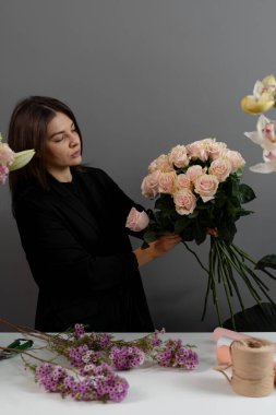 Gri arka plan çiçek stüdyosundaki çiçekçinin pembe güllerinden buket yapıyorum. Özel sipariş için çiçek bileşimi toplanıyor