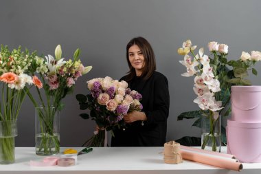 Gri arka plan çiçek stüdyosundaki çiçekçinin pembe güllerinden buket yapıyorum. Özel sipariş için çiçek bileşimi toplanıyor