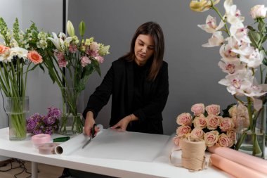 Çiçekçi çiçek aranjmanı için ambalaj kağıdını makasla kesiyor. Çiçek buketi yapmak için çiçek süsleme hazırlıyorum.